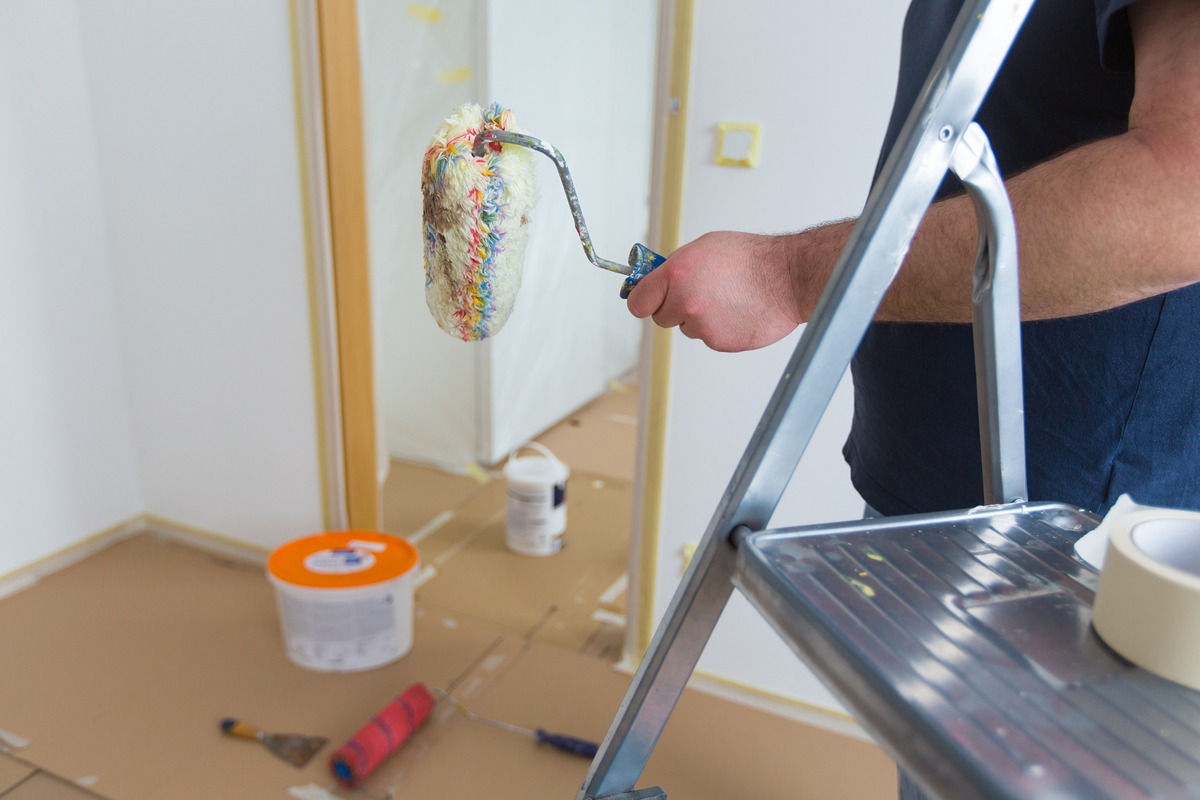recorte pintor con rodillo sobre fondo de habitacion cubierta por cartones